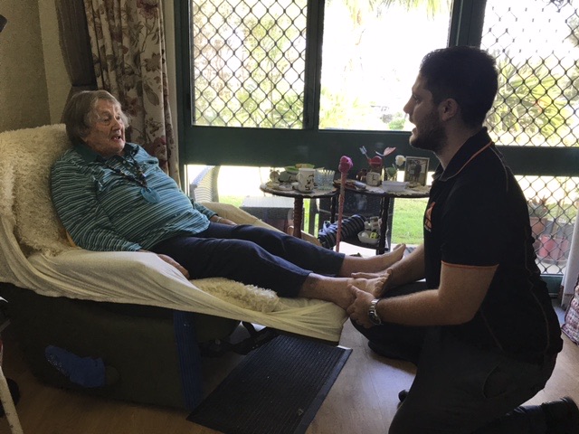Optimum physiotherapist treating an older client at home in her recliner