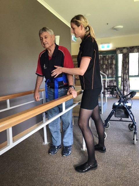 Client walking between parallel bars with physiotherapist support