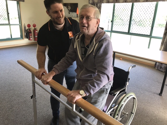 Older client standing at a support rail with an Optimum physiotherapist by his side