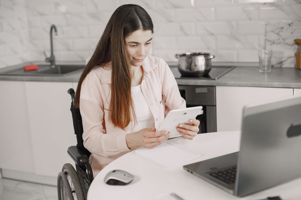 Woman using a wheelchair working on a tablet at her kitchen table